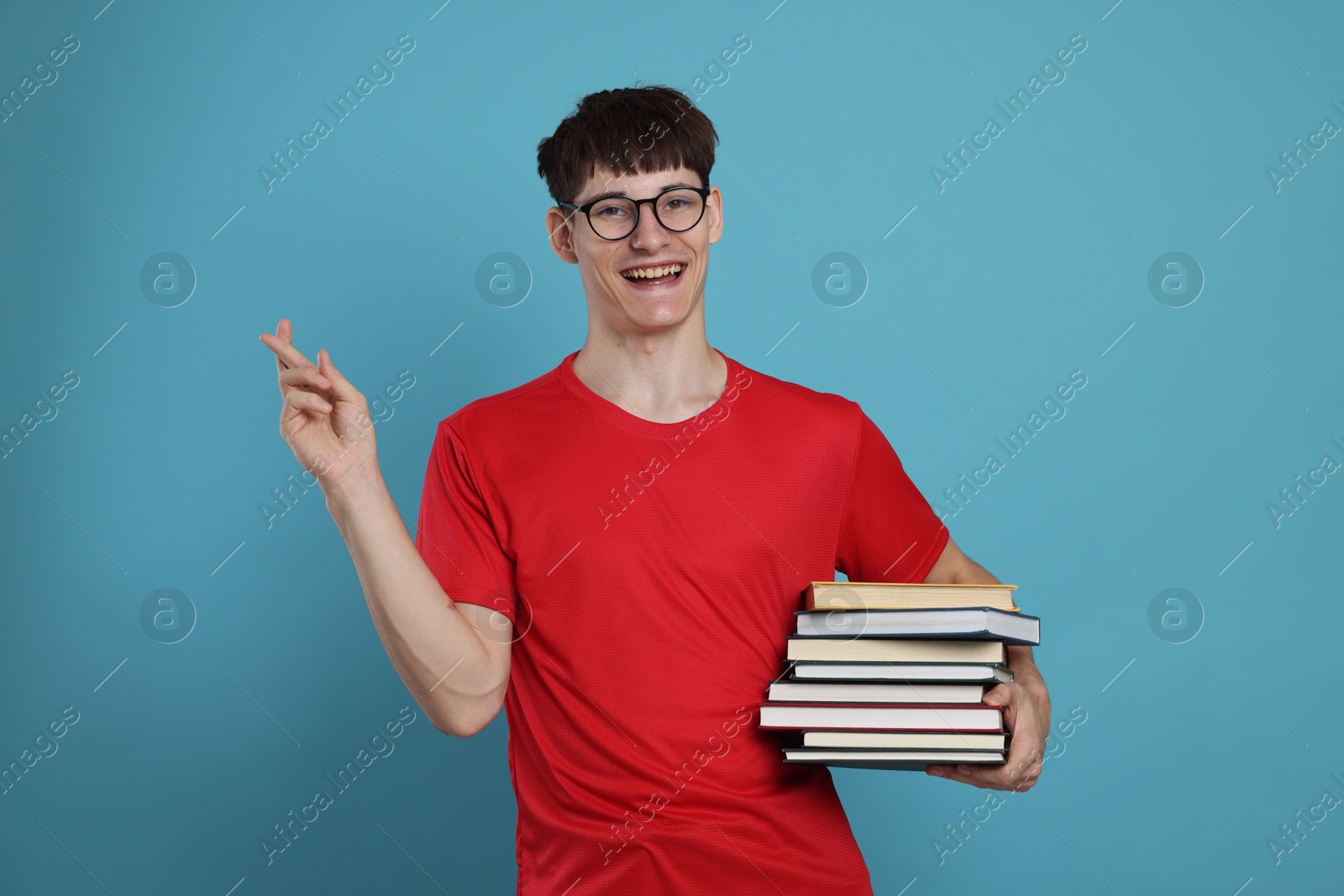 Happy student crossing fingers for good exam result on light blue background Photo of Happy student crossing fingers for good exam result on light blue background