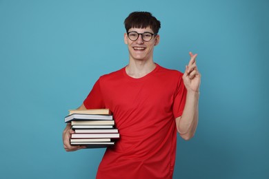 Photo of Happy student crossing fingers for good exam result on light blue background