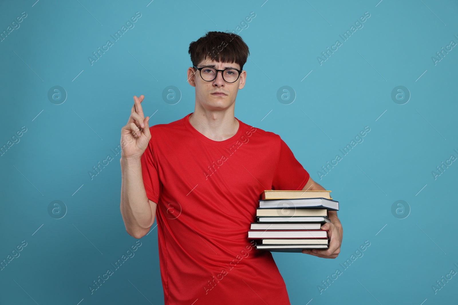 Worried student with books crossing fingers for good exam result on light blue background Photo of Worried student with books crossing fingers for good exam result on light blue background