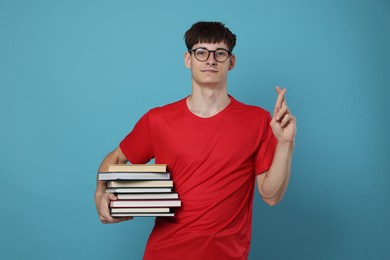 Photo of Worried student with books crossing fingers for good exam result on light blue background
