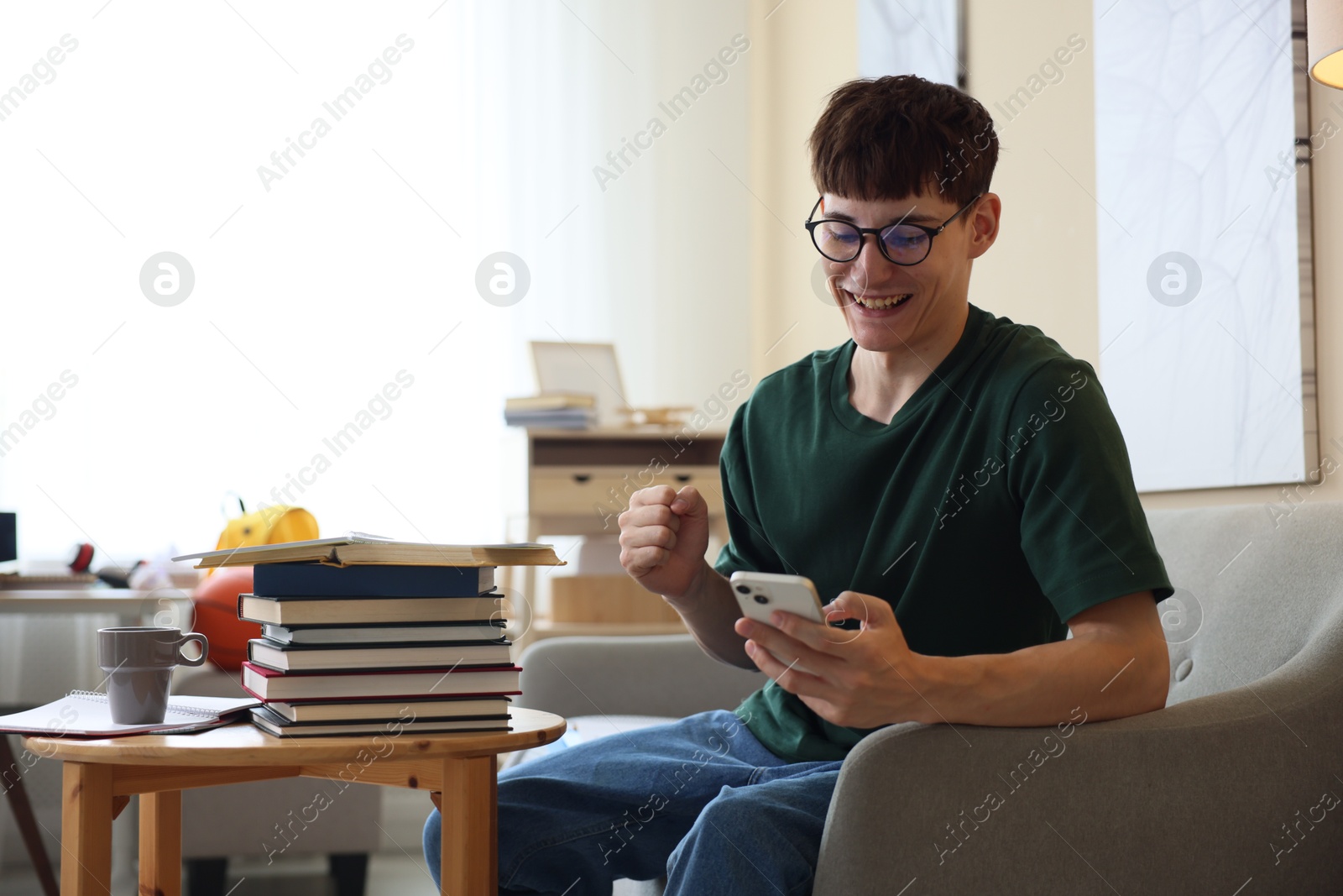 Happy student celebrating good exam result at table indoors Photo of Happy student celebrating good exam result at table indoors