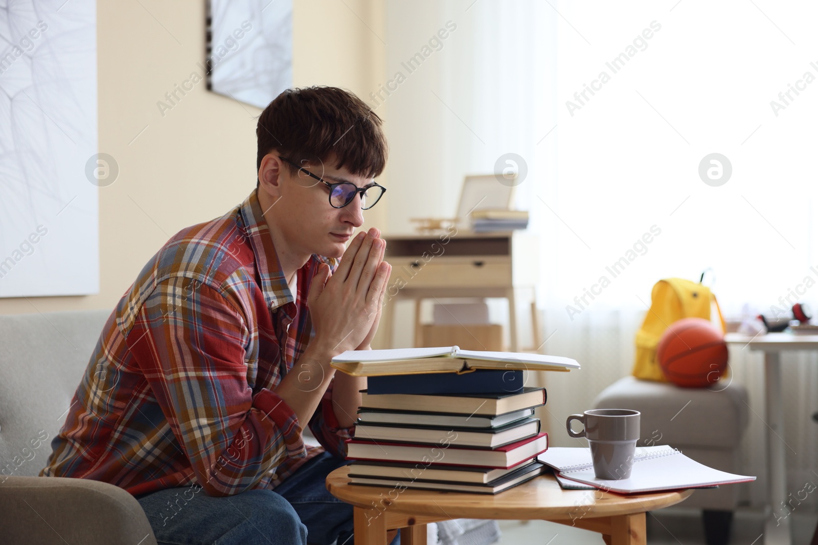 Worried student with clasped hands praying for good exam result at table indoors Photo of Worried student with clasped hands praying for good exam result at table indoors