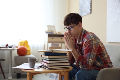 Photo of Worried student with clasped hands praying for good exam result at table indoors
