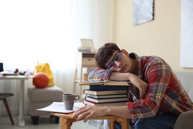 Photo of Tired student preparing for exam at table indoors