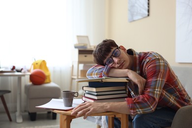 Photo of Tired student preparing for exam at table indoors