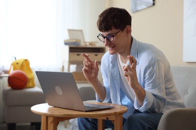 Photo of Happy student crossing fingers for good exam result at table indoors