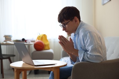 Photo of Worried student with clasped hands praying for good exam result at table indoors