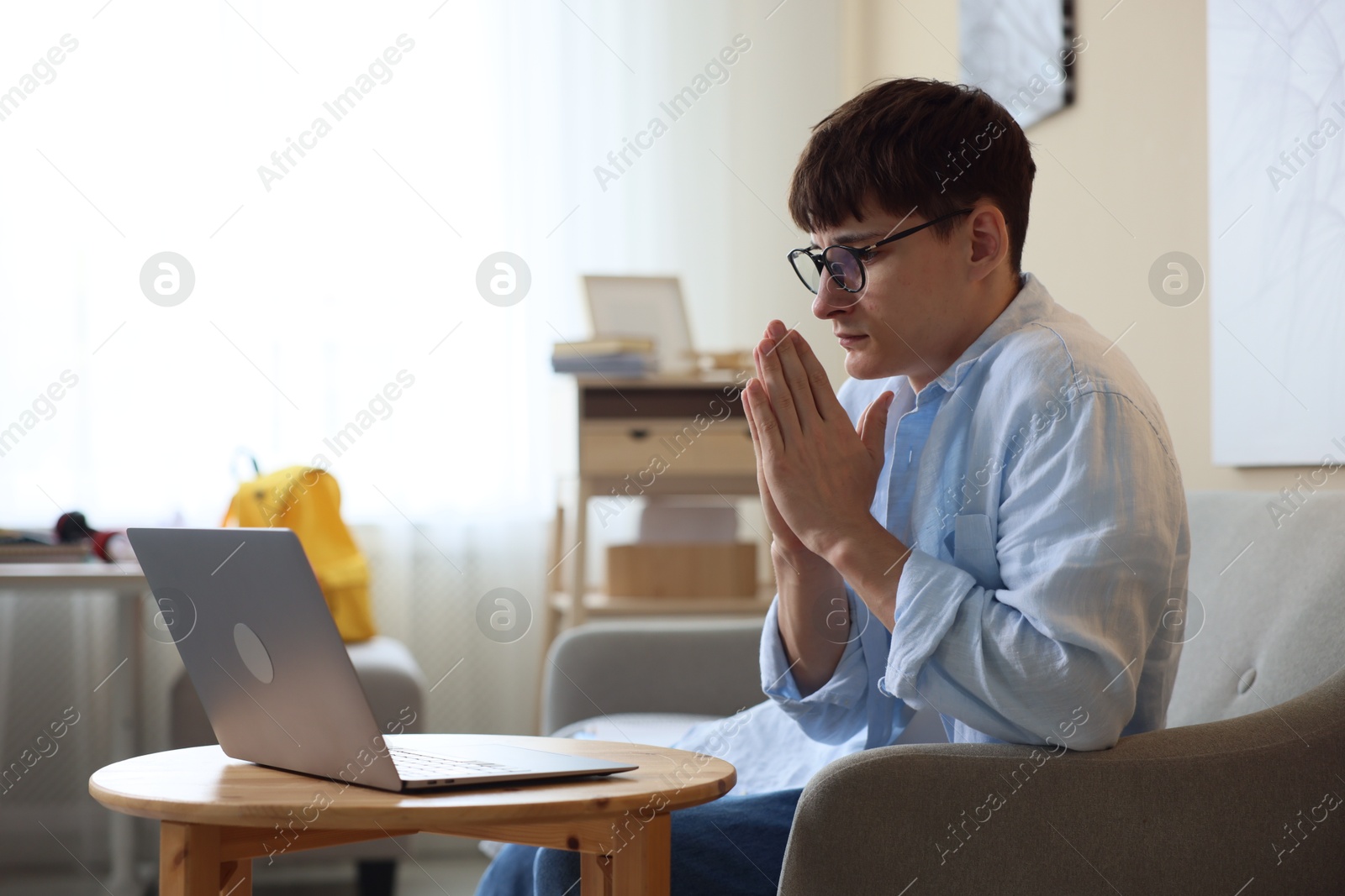 Worried student with clasped hands praying for good exam result at table indoors Photo of Worried student with clasped hands praying for good exam result at table indoors