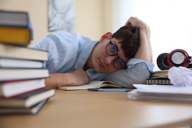 Photo of Tired student preparing for exam at table indoors