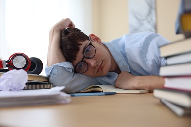 Photo of Tired student preparing for exam at table indoors