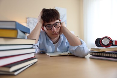 Photo of Tired student preparing for exam at table indoors