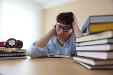 Photo of Tired student preparing for exam at table indoors