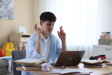 Photo of Worried student crossing fingers for good exam result at table indoors