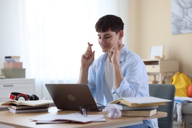 Photo of Worried student crossing fingers for good exam result at table indoors