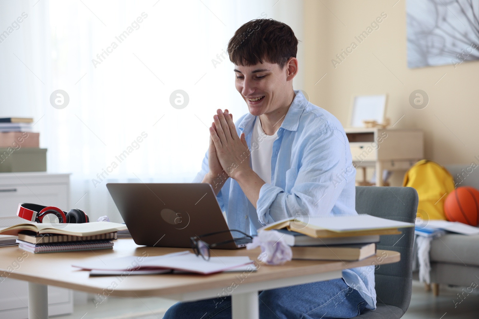 Happy student with clasped hands praying for good exam result at table indoors Photo of Happy student with clasped hands praying for good exam result at table indoors