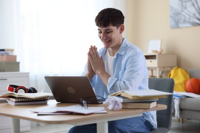 Photo of Happy student with clasped hands praying for good exam result at table indoors