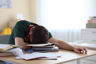 Photo of Tired student preparing for exam at table indoors