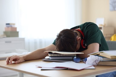 Photo of Tired student preparing for exam at table indoors