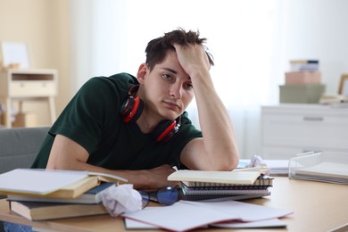 Photo of Tired student preparing for exam at table indoors