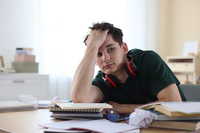 Photo of Tired student preparing for exam at table indoors