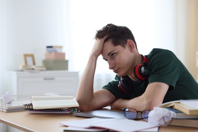 Photo of Tired student preparing for exam at table indoors