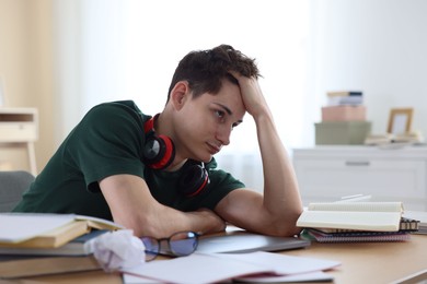 Photo of Tired student preparing for exam at table indoors