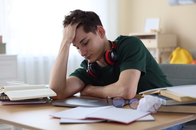 Photo of Tired student preparing for exam at table indoors