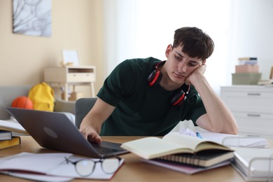 Photo of Tired student preparing for exam at table indoors