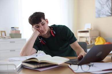 Photo of Tired student preparing for exam at table indoors