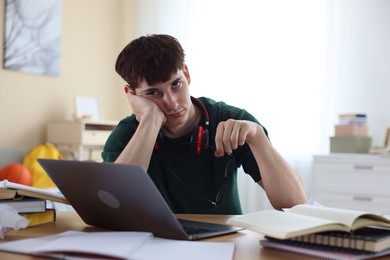 Photo of Tired student preparing for exam at table indoors