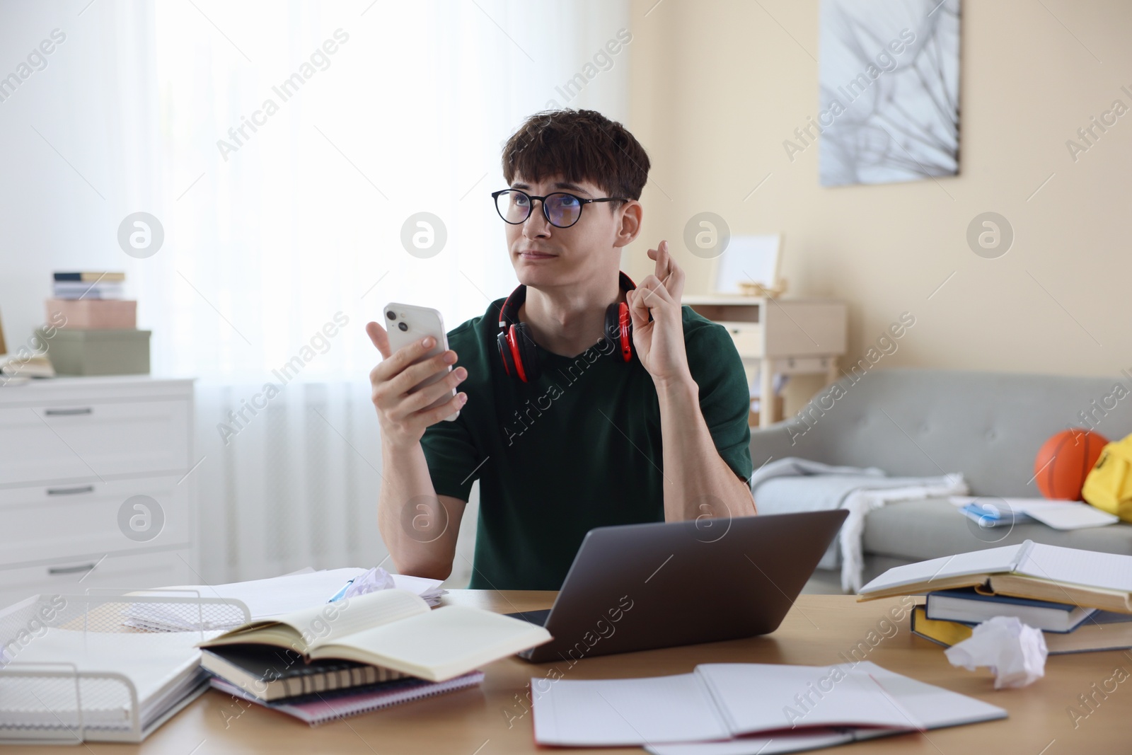Worried student crossing fingers for good exam result at table indoors Photo of Worried student crossing fingers for good exam result at table indoors