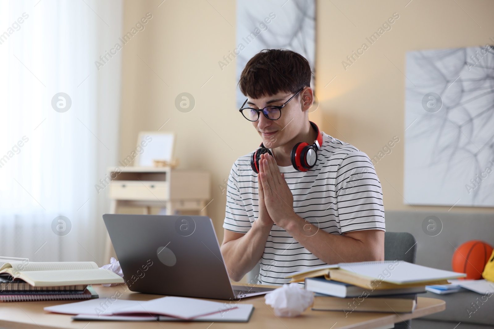 Worried student with clasped hands praying for good exam result at table indoors Photo of Worried student with clasped hands praying for good exam result at table indoors