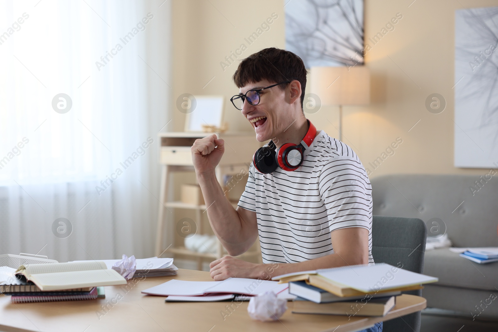 Happy student celebrating good exam result at table indoors Photo of Happy student celebrating good exam result at table indoors