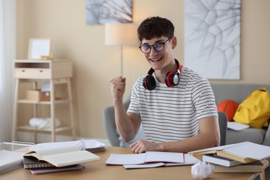 Photo of Happy student celebrating good exam result at table indoors