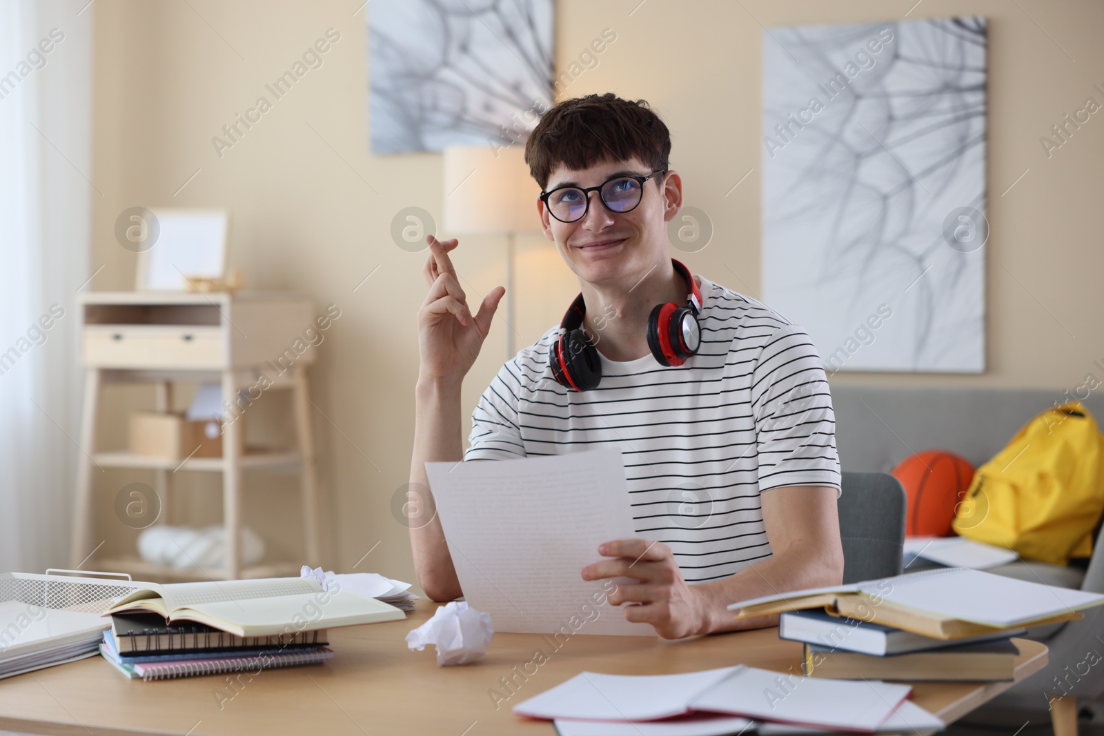 Happy student crossing fingers for good exam result at table indoors Photo of Happy student crossing fingers for good exam result at table indoors