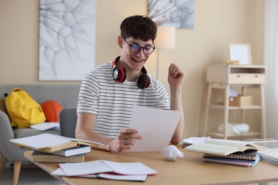 Photo of Happy student celebrating good exam result at table indoors