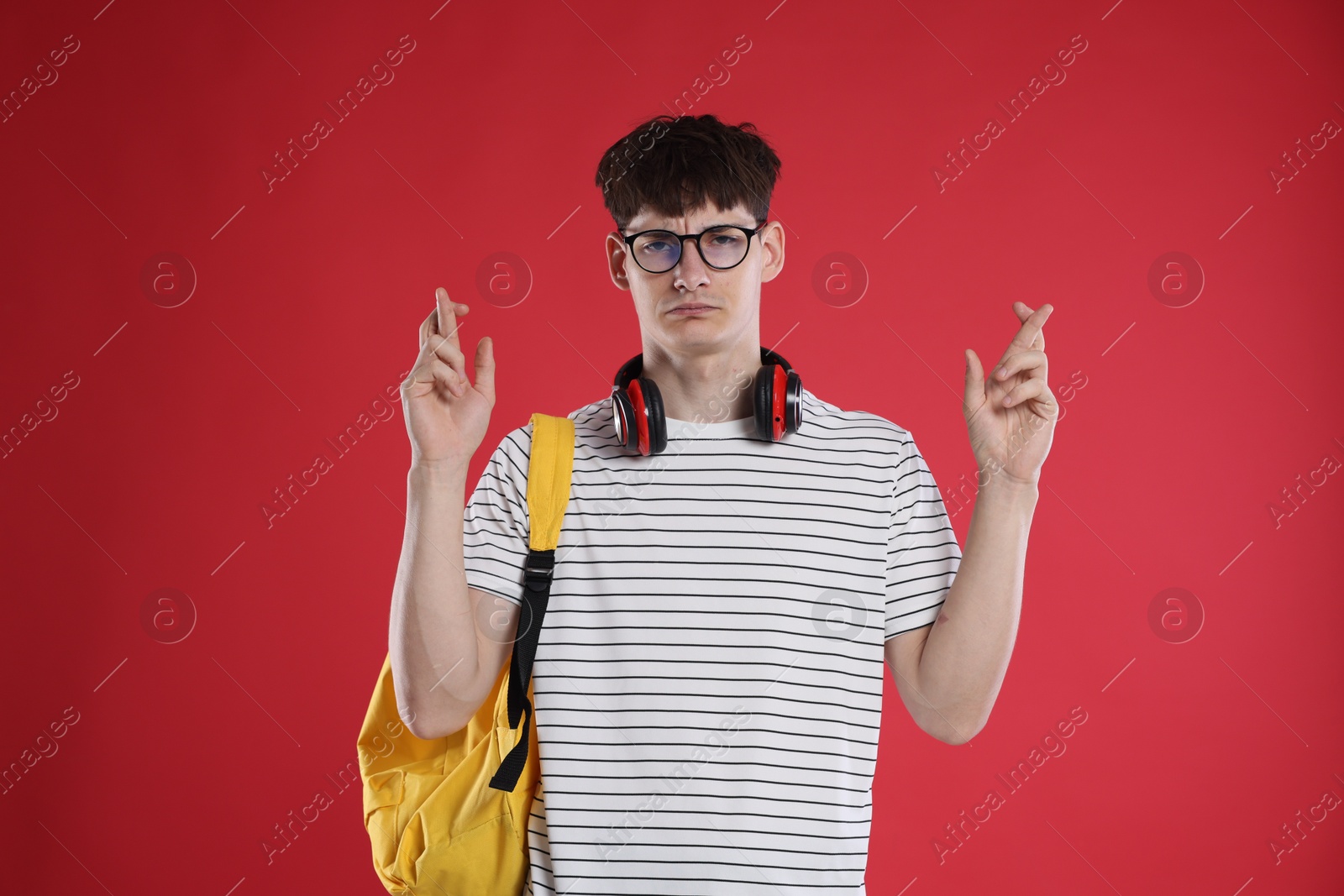 Worried student crossing fingers for good exam result on red background Photo of Worried student crossing fingers for good exam result on red background