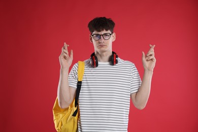 Photo of Worried student crossing fingers for good exam result on red background