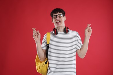 Photo of Happy student crossing fingers for good exam result on red background