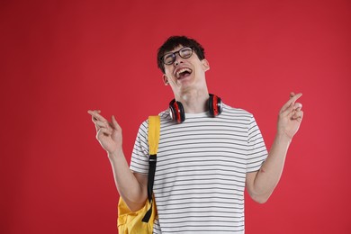 Photo of Happy student crossing fingers for good exam result on red background