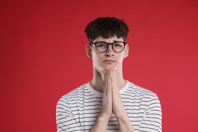 Photo of Worried student with clasped hands praying for good exam result on red background