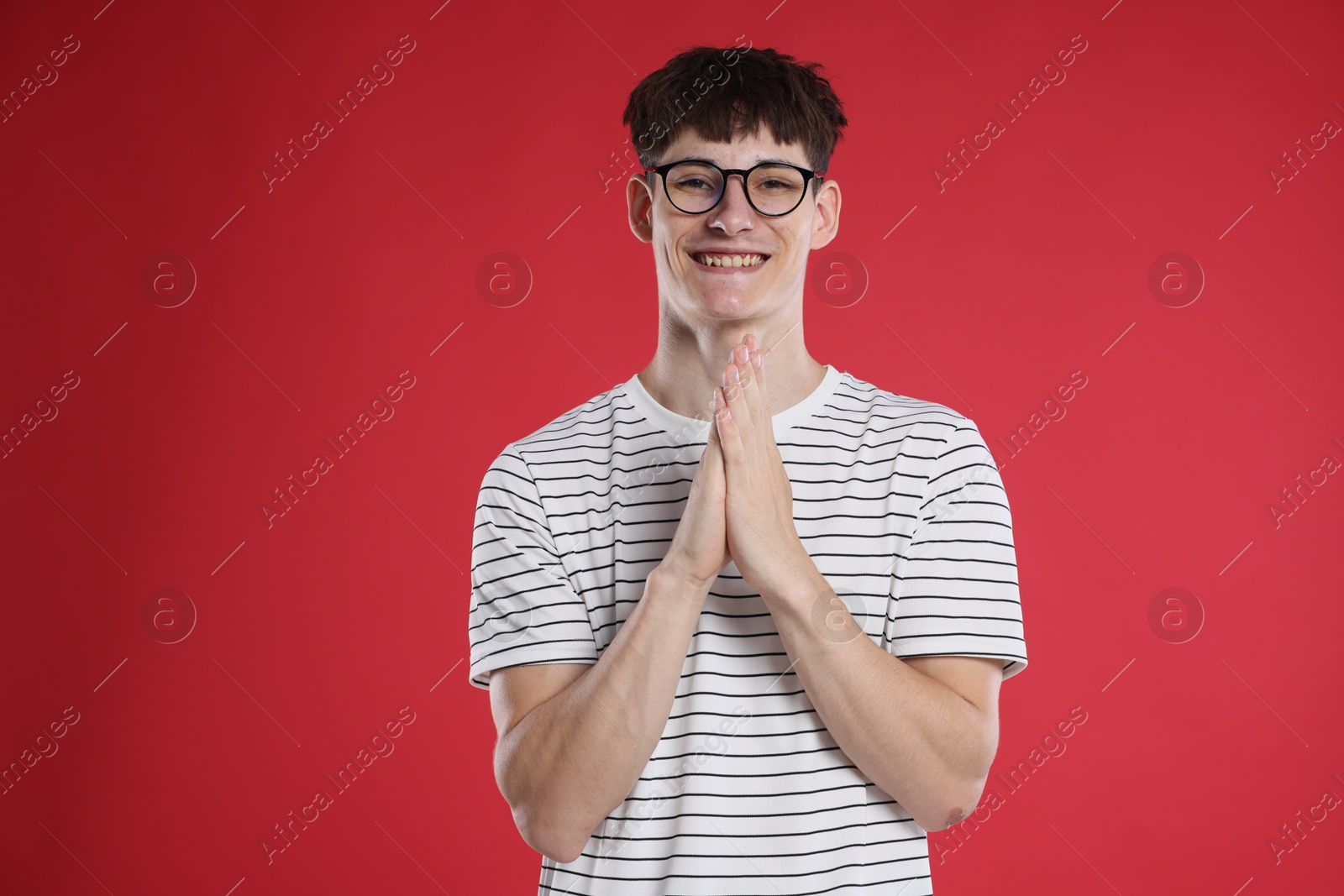 Happy student with clasped hands praying for good exam result on red background Photo of Happy student with clasped hands praying for good exam result on red background