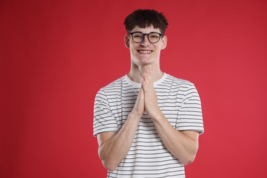 Photo of Happy student with clasped hands praying for good exam result on red background