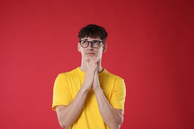 Photo of Worried student with clasped hands praying for good exam result on red background