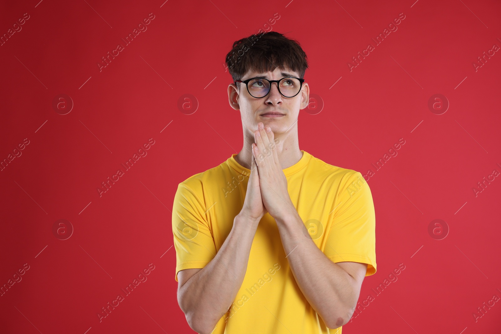 Worried student with clasped hands praying for good exam result on red background Photo of Worried student with clasped hands praying for good exam result on red background