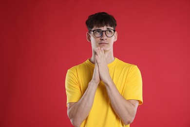 Photo of Worried student with clasped hands praying for good exam result on red background
