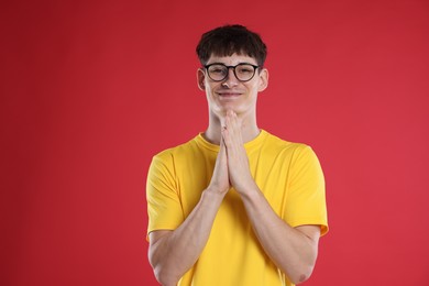 Photo of Happy student with clasped hands praying for good exam result on red background