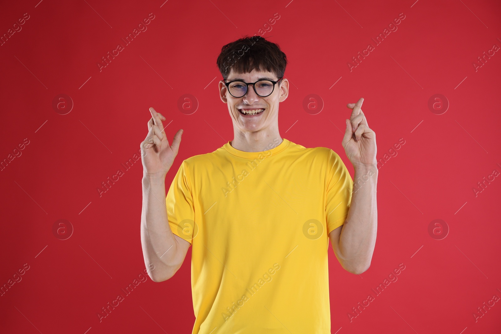 Happy student crossing fingers for good exam result on red background Photo of Happy student crossing fingers for good exam result on red background