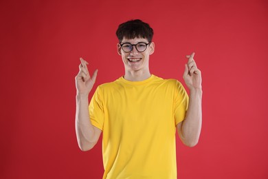 Photo of Happy student crossing fingers for good exam result on red background