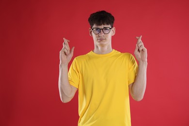 Photo of Worried student crossing fingers for good exam result on red background
